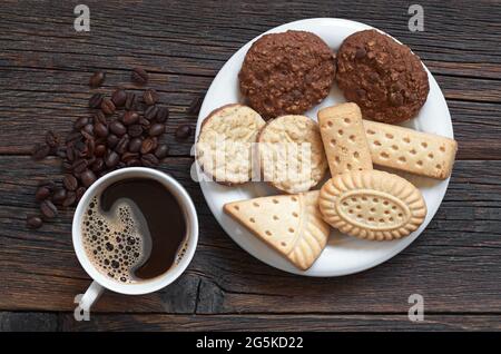 Tasse heißen Kaffee und verschiedene Shortbread-Kekse auf dem Teller auf dem alten Holztisch, Draufsicht Stockfoto