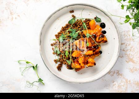 Salat mit gebackenem Kürbis, Linsen und Balsamico-Dressing, garniert mit Erbsen-Microgreens auf hellem Hintergrund. Gesundes veganes Essen, Draufsicht Stockfoto