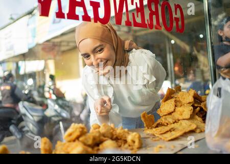 Ein schönes Mädchen in einem Schleier mit dem Finger zeigt, während die Wahl frittierte Lebensmittel Stockfoto