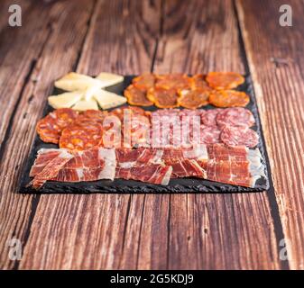 Food-Fotografie von Chorizo, Salami, Schinken, Käse und anderen Vorspeisen auf einem dunklen Brett. Typisch spanische Tapas-Mahlzeit auf einem Holztisch. Stockfoto