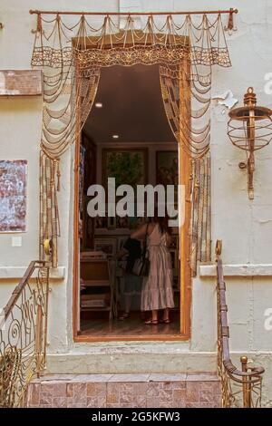 Öffnen Sie die Tür des Kunstshopfes in Tiflis, Georgien, umgeben von einem verzierten Metallvorhang und einem Treppengeländer, in dem Frauen einkaufen. Stockfoto