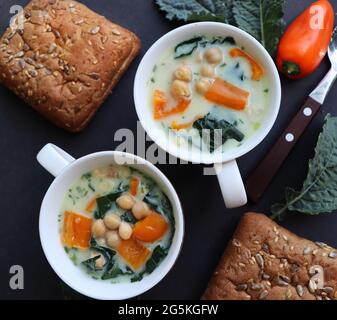 Weiße Suppe aus Kichererbsen, Grünkohl, Pfeffer und Kartoffeln in einer Schüssel auf dem dunklen Tisch. Draufsicht Stockfoto