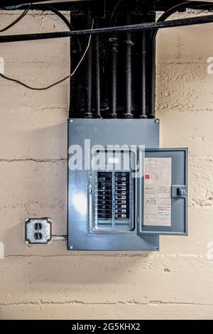 Der elektrische Schaltkasten aus Edelstahl ist geöffnet, und die Schaltkreise werden im Untergeschoss auf einer rauen Betonblockwand mit Kabelkanal und Decke und anderem pi von Hand benannt Stockfoto