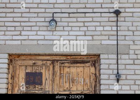 Alte Nacht-Sicherheitslampe aus Metall und Glas über einer bemalten Holztür an einer Ziegelwand. Stockfoto