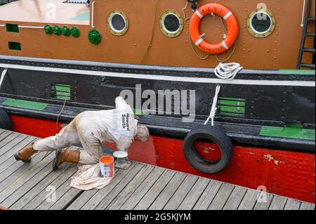 Ein Freiwilliger der South Eastern Tug Society malte den Rumpf des M.T. Kent-Schleppers, während er an der Chatham Maritime Marina, Kent, England, festgemacht wurde. Stockfoto