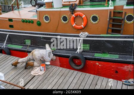 Ein Freiwilliger der South Eastern Tug Society malte den Rumpf des M.T. Kent-Schleppers, während er an der Chatham Maritime Marina, Kent, England, festgemacht wurde. Stockfoto