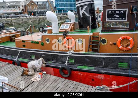 Ein Freiwilliger der South Eastern Tug Society malte den Rumpf des M.T. Kent-Schleppers, während er an der Chatham Maritime Marina, Kent, England, festgemacht wurde. Stockfoto