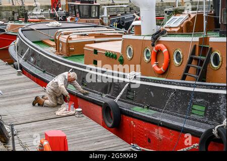 Ein Freiwilliger der South Eastern Tug Society malte den Rumpf des M.T. Kent-Schleppers, während er an der Chatham Maritime Marina, Kent, England, festgemacht wurde. Stockfoto