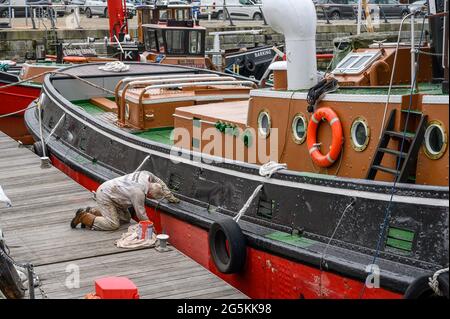 Ein Freiwilliger der South Eastern Tug Society malte den Rumpf des M.T. Kent-Schleppers, während er an der Chatham Maritime Marina, Kent, England, festgemacht wurde. Stockfoto