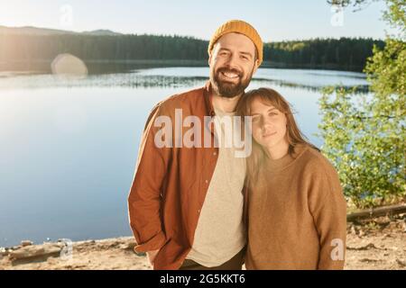 Porträt eines jungen Paares, das lächelt und die Kamera in der Nähe des Sees anschaut und ihre Reise genießt Stockfoto