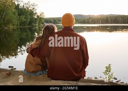 Rückansicht eines Paares in warmer Kleidung, das die wunderschöne Aussicht auf den See im Freien umarmt und genießt Stockfoto