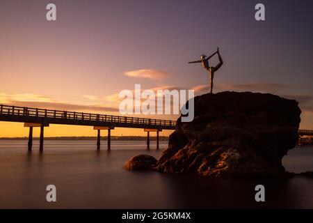 Die Statue Grace auf dem „Meteor“ führt die Natarajasana-Yoga-Pose unter dem Sonnenuntergang entlang des Boardwalk am Boulevard Park in Bellingham, WA, durch. Stockfoto