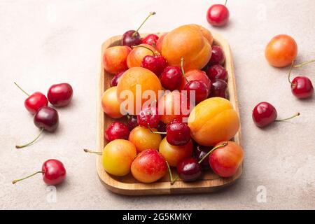 Bio-Früchte und Beeren auf einem Holzteller. Saftige Kirschen, Pflaumen und Aprikosen auf hellem Hintergrund Stockfoto