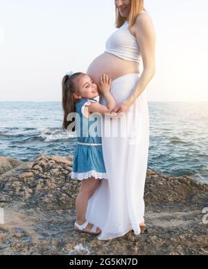 Schöne Tochter, die dem Herzschlag des zukünftigen Babys lauscht Stockfoto