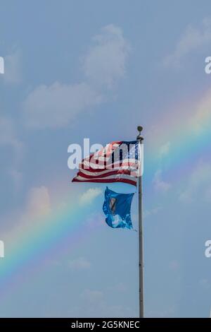 Flaggen der Vereinigten Staaten und Oklahoma fliegen hoch vor dem Regenbogenhimmel mit ein paar Wolken Stockfoto