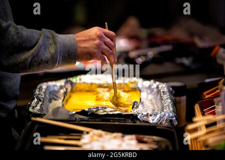 Nahaufnahme von Tamagoyaki, japanischen Eiern, die Omelette gerollt haben, auf der Einzelhandelsauslage in Kyoto, Japan, Nishiki Market Street, mit Person, die einen Teil des Omelettes serviert Stockfoto