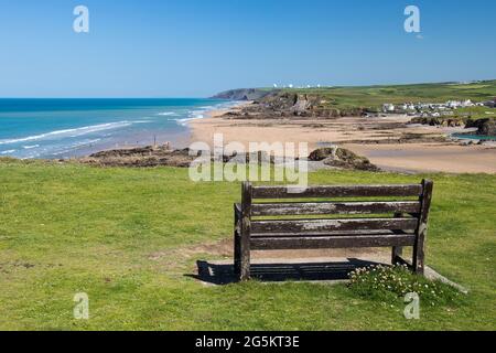 Holzbank mit Blick auf das Meer und den strand von crooklets in Bude, Nord-Cornwall, an einem sonnigen Tag mit blauem Himmel. Stockfoto