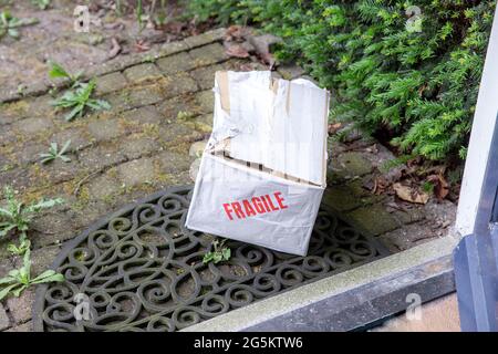 Beschädigter Lieferkarton an der Haustür eines Hauses, zerbrechliches Paket mit Beulen, schlechtes Lieferkonzept Stockfoto