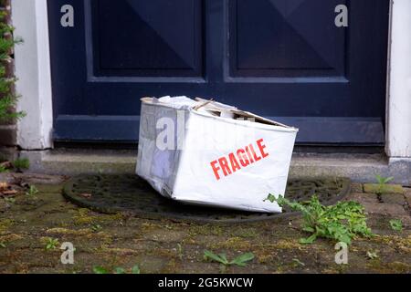 Beschädigter Lieferkarton an der Haustür eines Hauses, zerbrechliches Paket mit Beulen, schlechtes Lieferkonzept Stockfoto