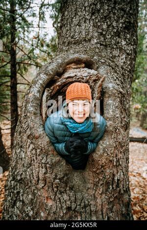 Frau mit Hut lächelt und lacht in einem großen Baumknoten Stockfoto