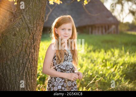 Junges Mädchen mit roten Haaren, die am Baum stehen, Scheune im Hintergrund. Stockfoto