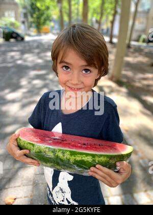 Kleiner Junge, der eine Wassermelone trägt Stockfoto