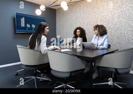 Multikulturelle Geschäftsfrauen in formeller Kleidung sitzen während einer Besprechung auf einem großen Schreibtisch. Stockfoto