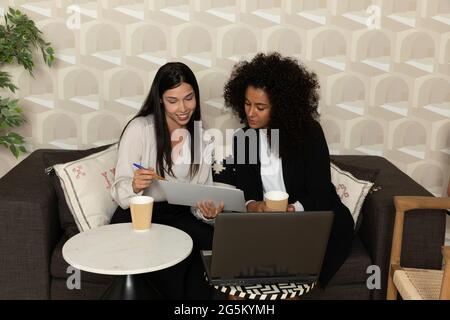 Glückliche schwarze Frau, die im Büro auf einer Couch sitzt und mit ihrem Kollegen spricht. Bürokonzept. Stockfoto