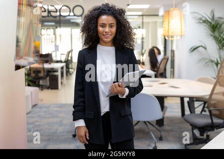Lächelnde junge Geschäftsfrau, die Papierarbeit hält und lächelt und die Kamera anschaut. Stockfoto