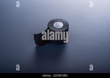 Das medizinische Klebeband liegt auf einem schwarzen Hintergrund. Schwarze Rolle Kineziotape. Sport-Patch, entwickelt, um Muskeln, Gelenke und Ausfluss der Lymphe zu erhalten. Stockfoto