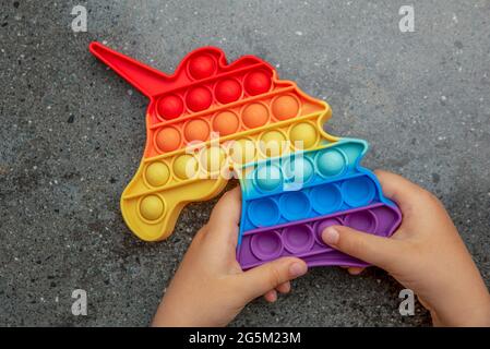 Pop it Spielzeug, Regenbogenfarben, in Form eines Einhorns. Farbenfrohe, bunte, sensorische Anti-Stress-Spielzeug Fidget Pop es in die Hände der Kinder. Stockfoto