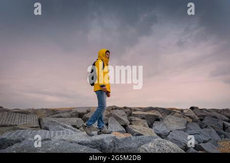 Frau mit einem gelben wasserdichten Mantel, die bei schlechtem Wetter über Felsen läuft. Stockfoto