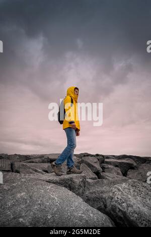 Frau mit einem gelben wasserdichten Mantel, die bei schlechtem Wetter über Felsen läuft. Stockfoto