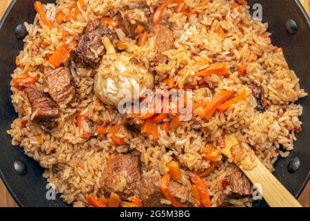 Nahaufnahme des Pilafs. Konzept der orientalischen Küche. Nationaler usbekischer Pilaf mit Fleisch in einer gusseisernen Pfanne. Draufsicht, Lamm, Devzira-Reis. Stockfoto