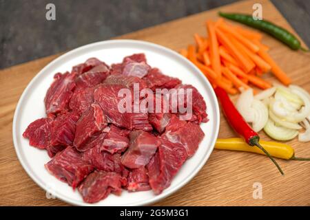 Kochen von Pilaf in einem Kessel, ein Rezept für echten Pilaf. Zutaten zum Kochen Pilaf auf einem Holzhintergrund. Zwiebeln, Paprika, Karotten, Hackfleisch liegen Stockfoto