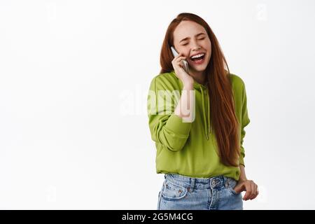 Portrait eines modernen ehrlichen Mädchens, lächelnd und lachend, natürliche Pose beim Telefonieren, mit einem Freund auf dem Smartphone lachen, reden und Spaß haben Stockfoto