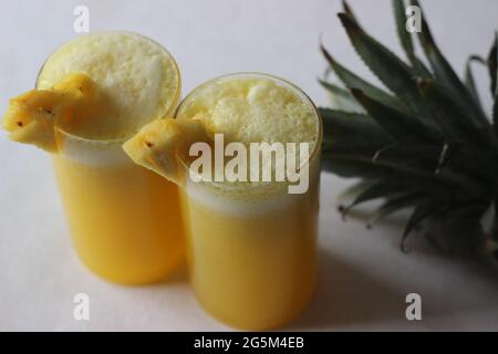 Gekühlter Ananassaft, um die Sommerhitze zu überbieten. Hausgemachter Saft, serviert in einem langen Glas, das mit einem Ananaskeil verziert ist. Aufgenommen auf weißem Hintergrund Stockfoto