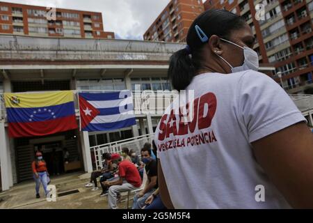 Caracas, Venezuela. Juni 2021. Die Menschen warten vor einem Establishment mit der venezolanischen und kubanischen Flagge auf seiner façade, wo sie den kubanischen Corona-Impfstoff Abdala erhalten sollen. Die erste Lieferung von Impfstoffen aus Kuba wird 10,000 Menschen in Venezuela die erste Dosis des Impfstoffs geben, so die kubanischen Behörden. Kredit: Jesus Vargas/dpa/Alamy Live Nachrichten Stockfoto