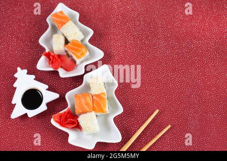 Sushi auf einem Teller als Weihnachtsbaum auf festlichem Hintergrund. Blick von oben. Platz für Text. Flatlay-Style. Stockfoto