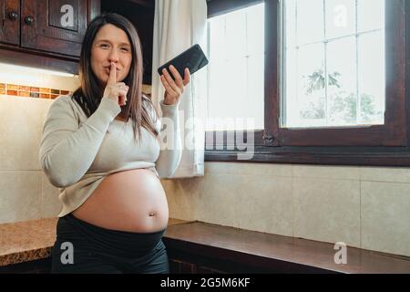 Hispanische Schwangere bittet um Stille, während sie Audio auf dem Handy aufzeichnet Stockfoto