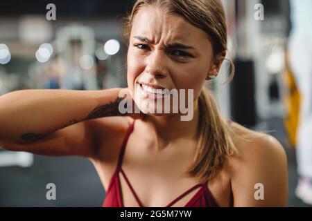 Unglückliche sportliche Sportlerin mit Nackenschmerzen beim Training im Fitnessstudio Stockfoto