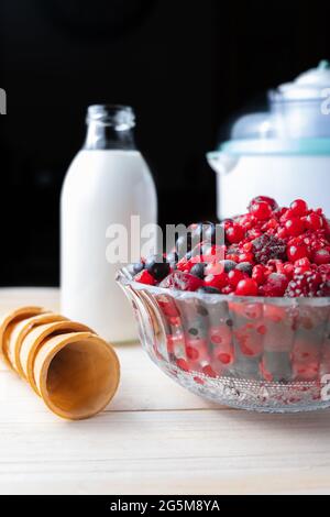 Vertikales Foto eines Holztisches mit den Zutaten für die Herstellung von hausgemachtem Eis: Rote Beeren, Creme, Eiscreme und Eiszapfen Stockfoto