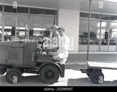 1957, historisches Ferienlager Prestatyn, außerhalb des Essbereichs, ein Pärchen, das auf einem kleinen Geländewagen mit Anhänger sitzt. Das Ferienzentrum in Prestatyn, Wales, wurde 1939 von der London Midland and Scottish Railway Co. Erbaut, wobei die Hauptgebäude im Stil von 1930s mit abgerundeten Gebäudeenden und Fenstern mit Stahlrahmen ausgestattet sind. Stockfoto