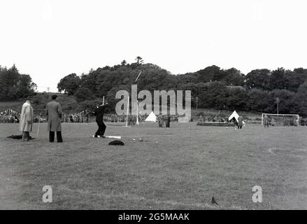 1956, historische, schottische Hochlandspiele, Mann, der den Hammer warf, beobachtet von zwei Beamten in Mänteln. Es werden keine Kilts angezeigt. Stockfoto