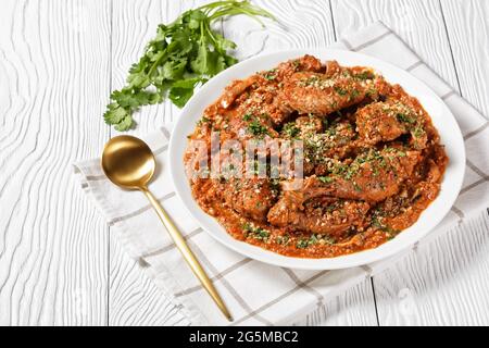 Chakhokhbili, geschmortes Huhn, Tomate mit frischen Kräutern, Walnüssen und Gewürzen auf einer weißen Platte auf einem Holztisch, georgische Küche Stockfoto