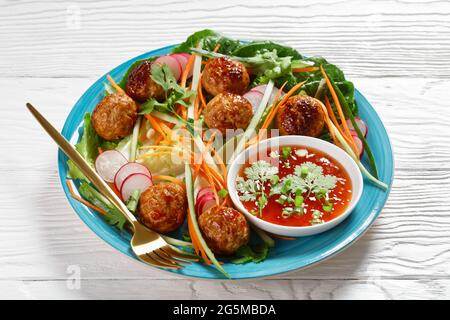 Vietnamesischer Banh-mi-Salat mit Fleischbällchen, Karotten, Gurken und Rettich, serviert über Salat mit Rosenkohm auf einem blauen Teller mit süßer Chilisauce Stockfoto