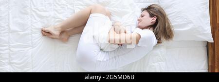 Junge Frau liegt im Bett und hält sich an Wunde Bauchansicht von oben Stockfoto