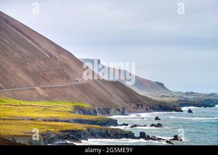 Island Berge Landschaftsansicht der Ringstraße Autobahn, braune felsige Bergklippe an bewölktem Tag im Osten Süd-Südosten mit Atlantischem Ozeanwasser Stockfoto