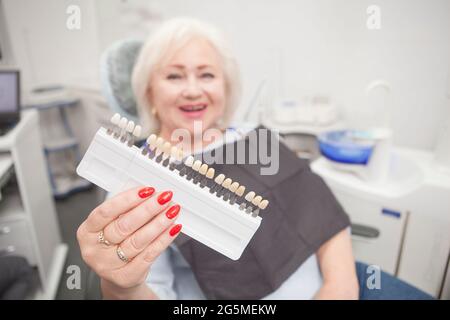 Ältere Frau lachend, hoding aus Zähne Aufhellung Farbtafel an die Kamera in der Zahnklinik Stockfoto