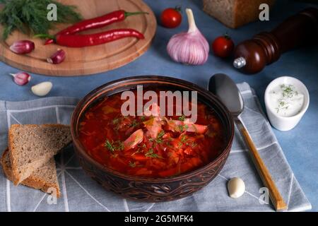 Nahaufnahme des traditionellen russischen Suppenborschts aus Kohl, Rüben und anderem Gemüse, serviert auf einer Tontafel aus Keramik mit Sauerrahm und Garl Stockfoto